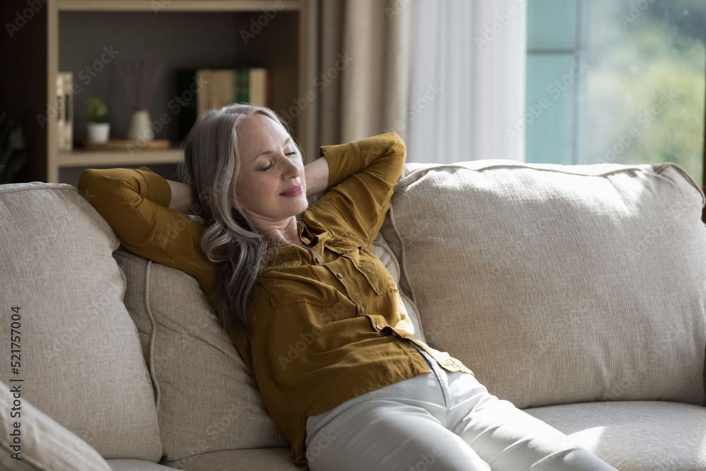Peaceful happy sleepy elderly homeowner woman sitting on soft couch with closed eyes, stretching body, enjoying comfort, leisure time at home, meditating, taking deep breath of fresh air Peaceful happy sleepy elderly homeowner woman sitting on soft couch with closed eyes, stretching body, enjoying comfort, leisure time at home, meditating, taking deep breath of fresh air