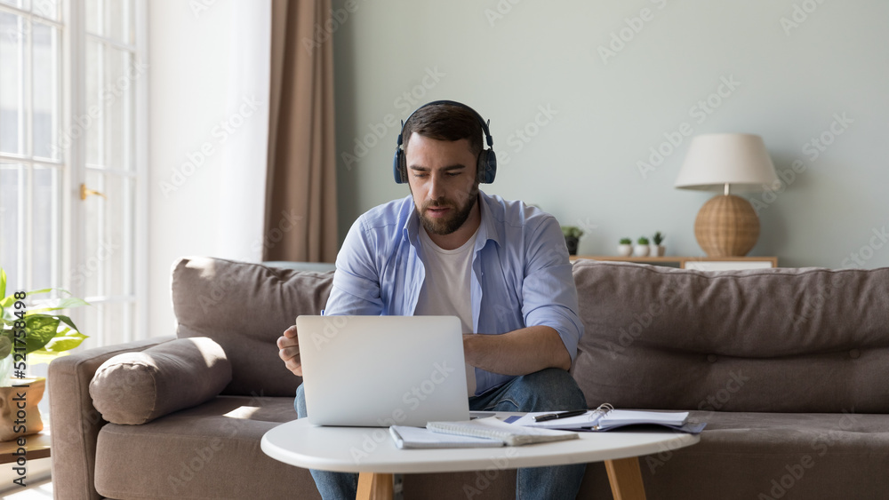 Man in wireless headphones looks at laptop communicates to client provide counsel help distantly use videoconference application. Education, e-learning, audio course to improve language skills concept Man in wireless headphones looks at laptop communicates to client provide counsel help distantly use videoconference application. Education, e-learning, audio course to improve language skills concept