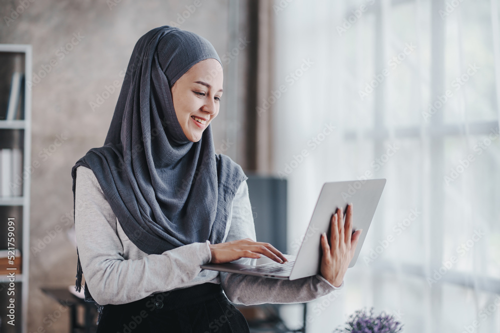 Muslim businesswoman holding a computer and typing smiling arab woman taking notes and work on laptop Muslim businesswoman holding a computer and typing smiling arab woman taking notes and work on laptop