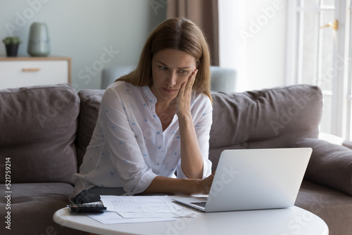 Concerned woman thinks over high domestic utility, huge electricity tariffs looks at laptop reviewing bank statement feels stressed due lack of money to pay bills. Expenses, financial problem concept