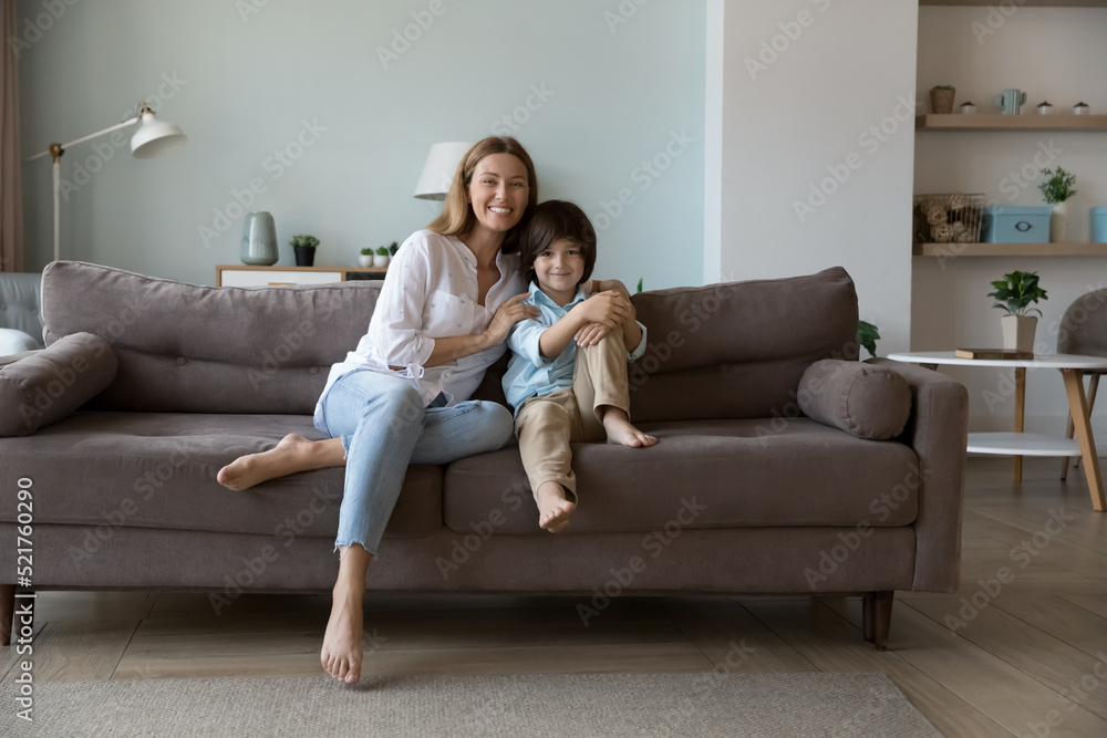 Young beautiful mother hugs little son posing on camera sit on couch, enjoy leisure together at home on weekend, having good friendly relations. Happy motherhood, custody, family bonding and cherish Young beautiful mother hugs little son posing on camera sit on couch, enjoy leisure together at home on weekend, having good friendly relations. Happy motherhood, custody, family bonding and cherish