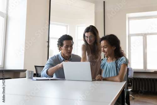 Three multiethnic teammates look at laptop screen prepare on-line presentation, working on corporate task, share skill and thoughts, analyse sales report, search solution. Business, teamwork concept © fizkes