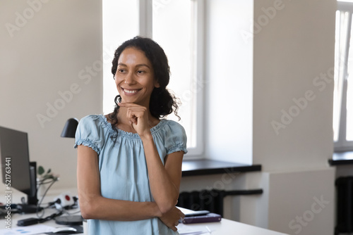 Smiling thoughtful African businesswoman pose indoor, staring into distance, thinking over project looks deep in thoughts, smile enjoy career and workday in modern office. Career, aspirations concept photo