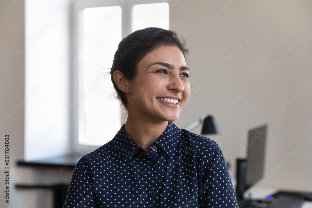 Head shot portrait happy Indian woman office employee. Company staff member hired millennial professional worker pose at workplace smile looks aside feels satisfied by career growth. Promotion concept Head shot portrait happy Indian woman office employee. Company staff member hired millennial professional worker pose at workplace smile looks aside feels satisfied by career growth. Promotion concept