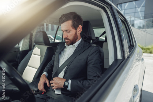 Handsome businessman is fastening his seat belt sitting in car