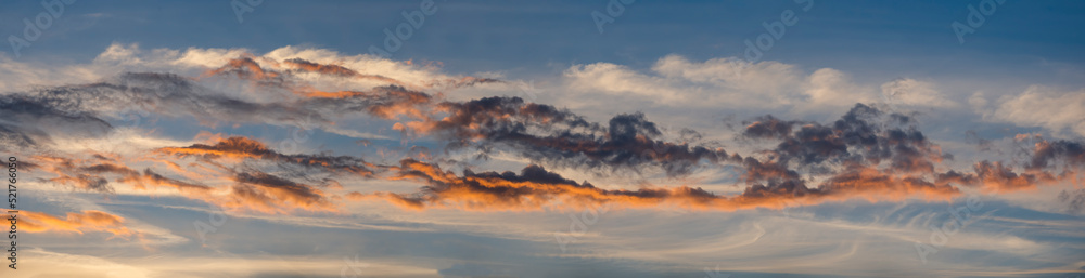 Panoramaaufnahme von der Sonne orange angestrahlten Wolkenbändern am blauen Abendhimmel