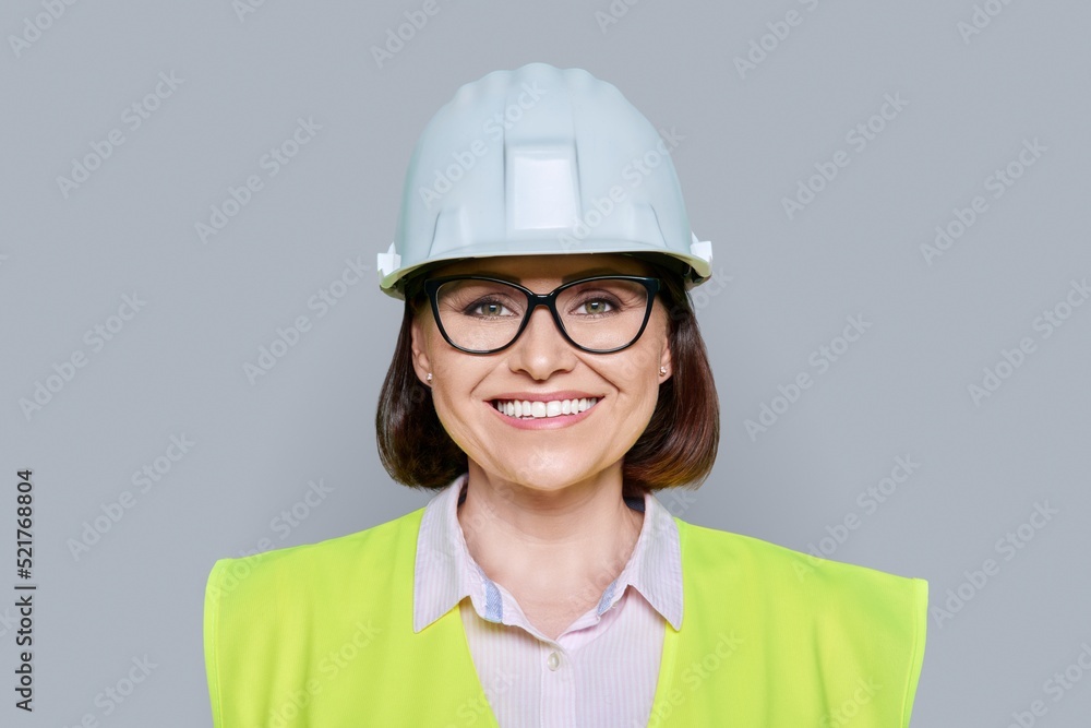 Female industrial worker in protective hard hat and vest on gray background