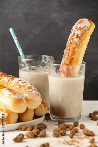 Close-up of glasses with horchata, on a white table with tiger nuts and fartons, gray background, vertical