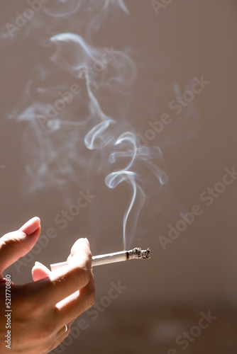Close-up of a woman's hand holding a cigarette. Tobacco butt with clouds of smoke. Nicotine addiction. The concept of the International Day of smoking cessation.
