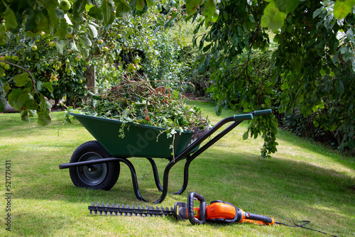 Fotobehang Gardening - Wheelbarrow full of hedge cuttings next to an electric hedge trimmer