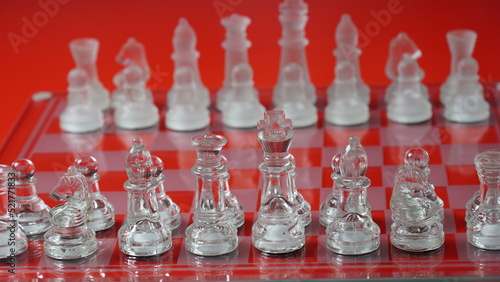 Transparent chess figures, on starting position, on reflective chess board, red tone. Strategic Chess board game