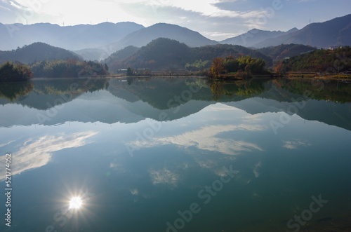 早朝の池に輝く太陽と連なる山々 © 展克 長谷川