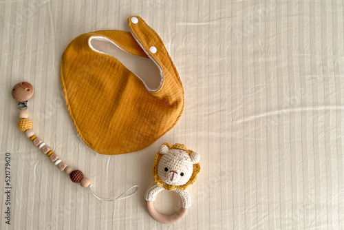 Composition with baby muslin bibs, rattles with a knitted bodice and chains of wooden beads with a nipple clothespin on a light background.