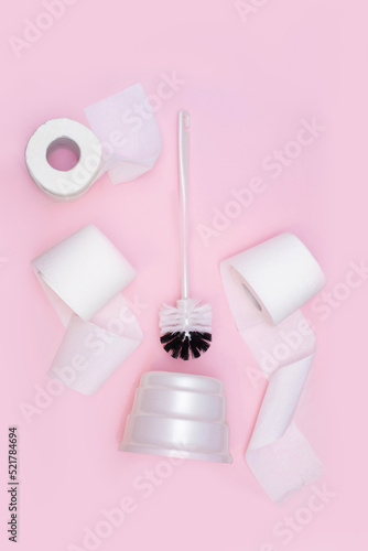 toilet brush and three rolls of toilet paper on a pink background