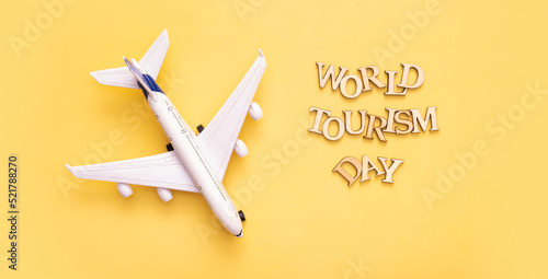 World Tourism Day text from wooden letters on a yellow background with airplane top view, flat lay photo