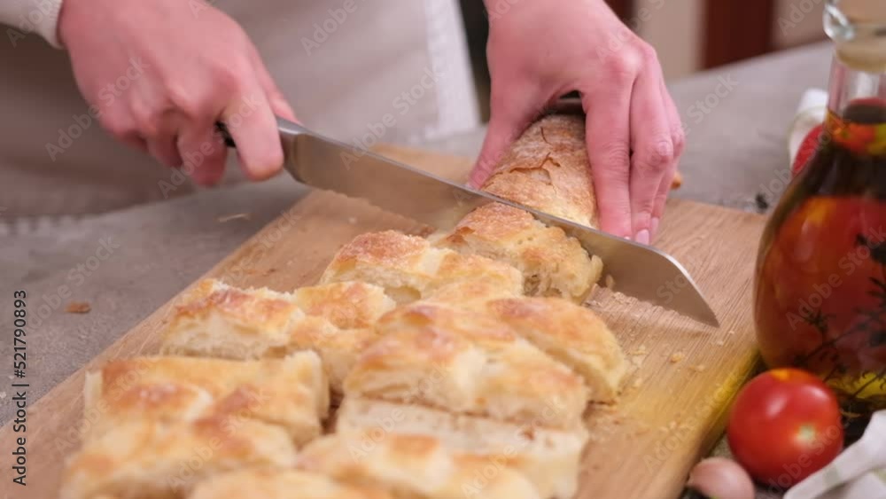 Woman slicing baguette on wooden cutting board at domestic kitchen Woman slicing baguette on wooden cutting board at domestic kitchen