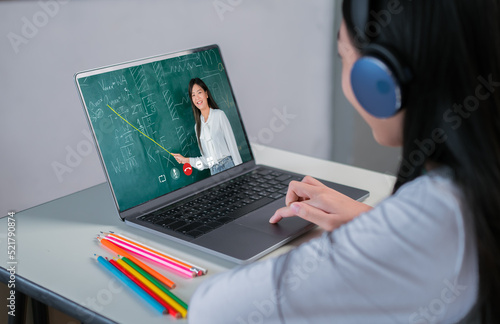 Rear view of asian girl student is learniing maths online classroom listening teacher, Female teacher teaching vocabulary by laptop computer at home using technology. photo