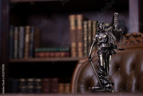 Law theme - judge office. Themis and gavel on the judge desk. Book shelf in the background.
