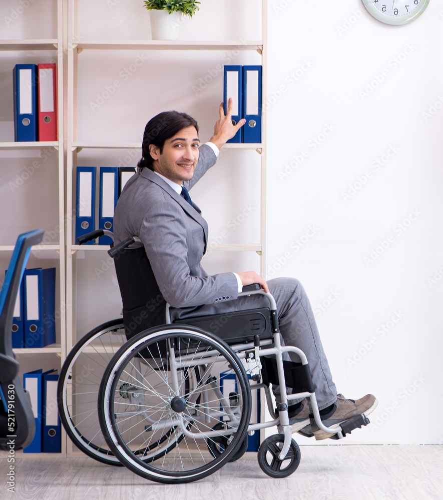 Young handsome employee in wheelchair working in the office Young handsome employee in wheelchair working in the office