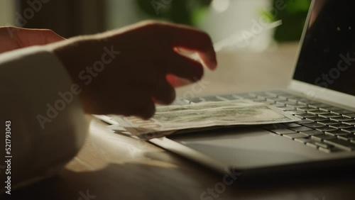 Handheld closee up of caucasian woman hands counting money 100 dollar bill on a laptop computer photo