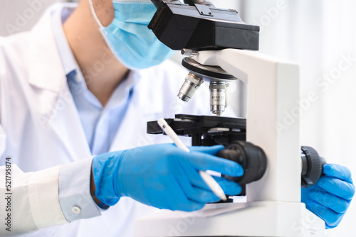 Scientist analyzing microscope slide at laboratory. Young woman technician is examining a histological sample, a biopsy in the laboratory of cancer research