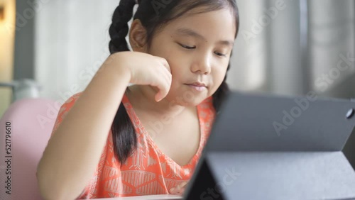 closeup asian child student enjoy studying online class on computer tablet or kid girl video call learning and smiling talking with suck candy taffy or person learn from home school in classroom photo