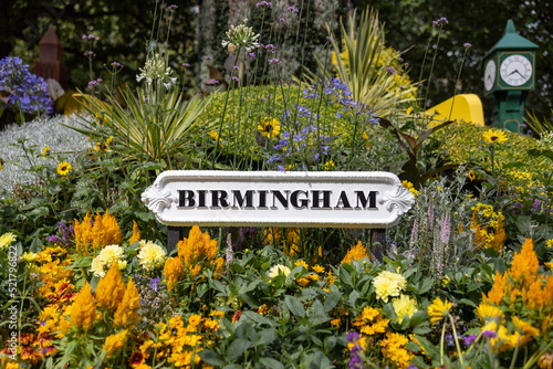 Birmingham city sign surrounded by flowers in garden of city centre park. Old black text on white background metal signage.