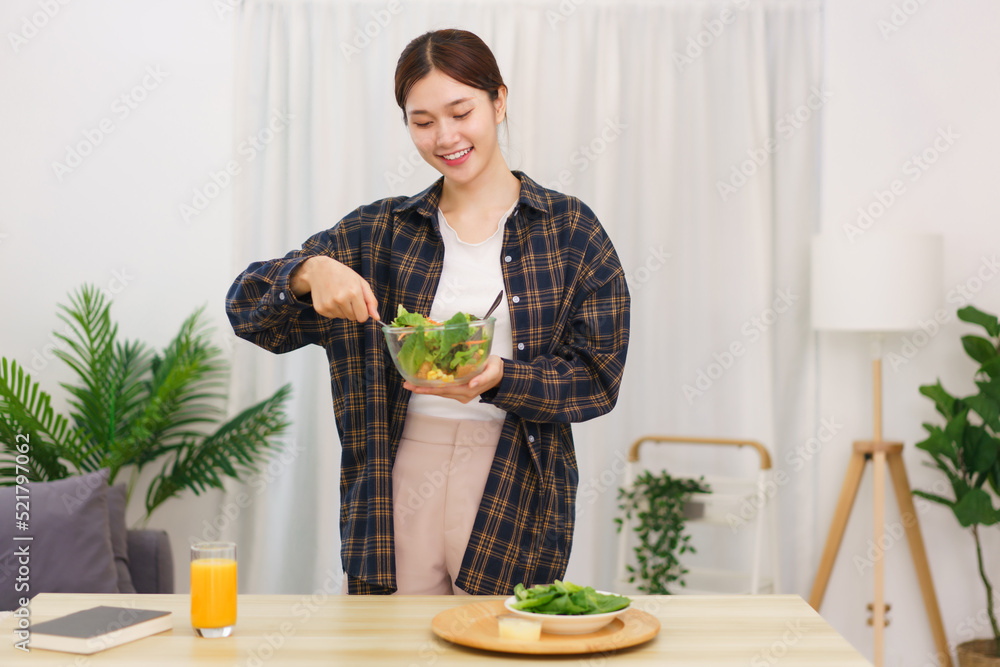 Lifestyle in living room concept, Young Asian woman standing to mixing vegetable salad in bowl Lifestyle in living room concept, Young Asian woman standing to mixing vegetable salad in bowl