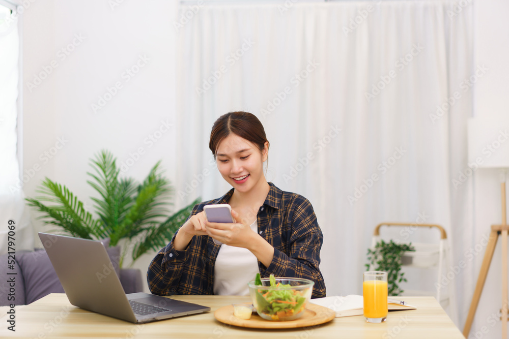 Lifestyle in living room concept, Young Asian woman using smartphone and eating vegetable salad Lifestyle in living room concept, Young Asian woman using smartphone and eating vegetable salad