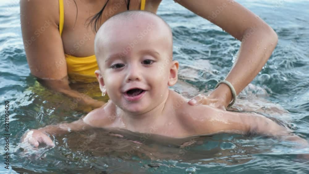 Handsome cute baby boy learning to swim in the sea, his mama is holding him. Handsome cute baby boy learning to swim in the sea, his mama is holding him.
