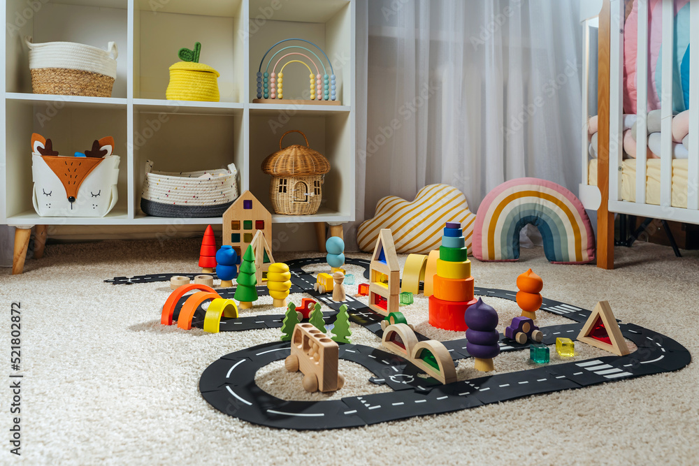 Fototapeta premium A toy town built in a children's room. Car track, toy cars, trees and wooden blocks for children's games in playroom. Educational game for baby and toddler in modern nursery.