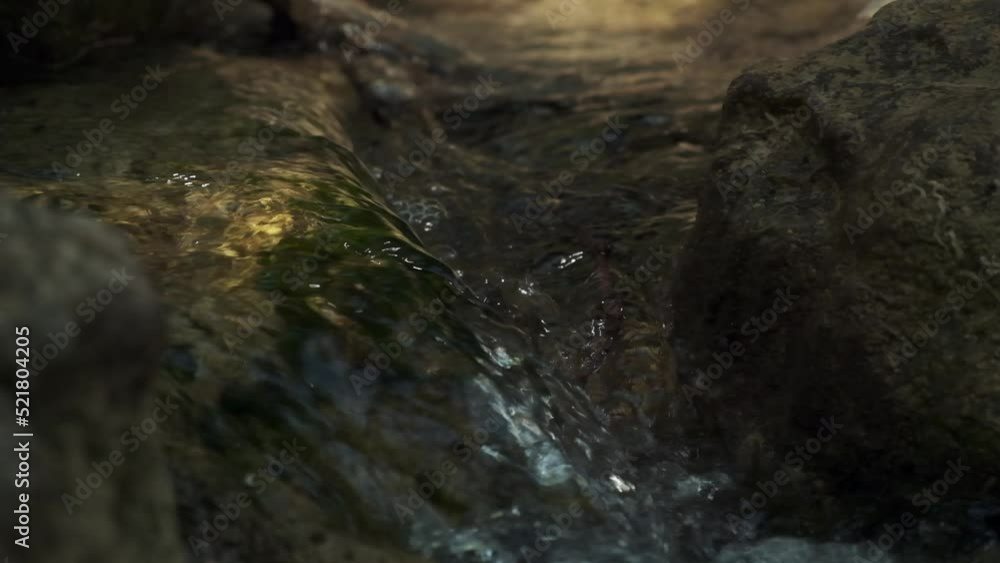 Slow motion closeup of a rushing stream, swift flow of spring water with some autumn colourful leaves in the water. Grey big stones, fallen autumnal leaves. Waterfall at fall. Slow motion closeup of a rushing stream, swift flow of spring water with some autumn colourful leaves in the water. Grey big stones, fallen autumnal leaves. Waterfall at fall.