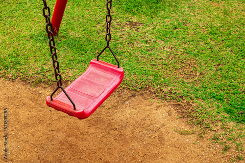 A red swing is attached to a rusty old chain in the playground. in the park saw the ground and the grass