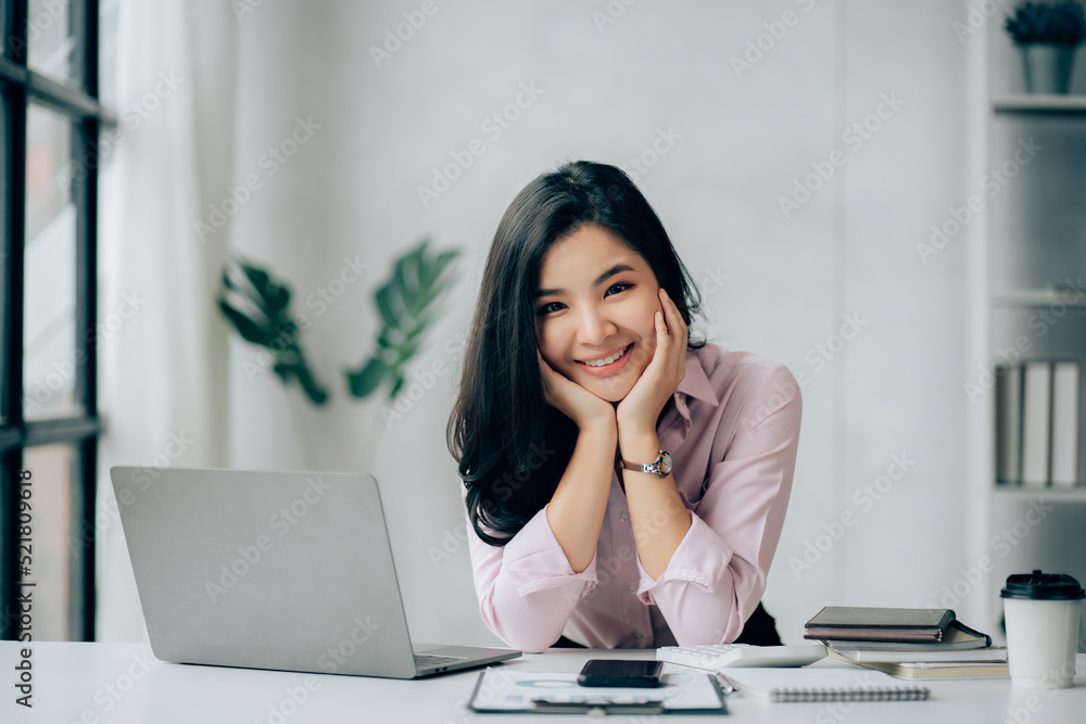 Charming Asian businesswoman working with a laptop at the office. Looking at camera