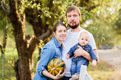 Portrait of Happy family hugging and spending time together outside in green nature. Young mother and father with little baby in garden. Apple harvest and picking on farm in autumn.