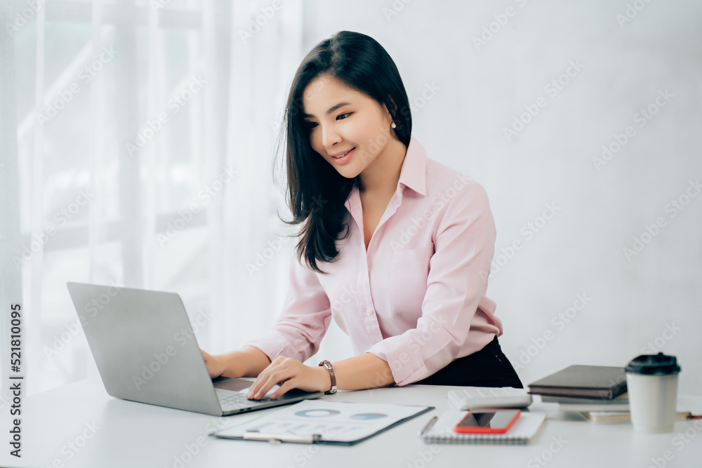 Happy young asian businesswoman sitting on her workplace in the office. Young woman working at laptop in the office Happy young asian businesswoman sitting on her workplace in the office. Young woman working at laptop in the office