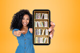 African woman pointing at phone with books on shelf, bright back