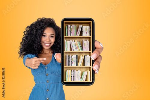 Stampa su tela African woman pointing at phone with books on shelf, bright back
