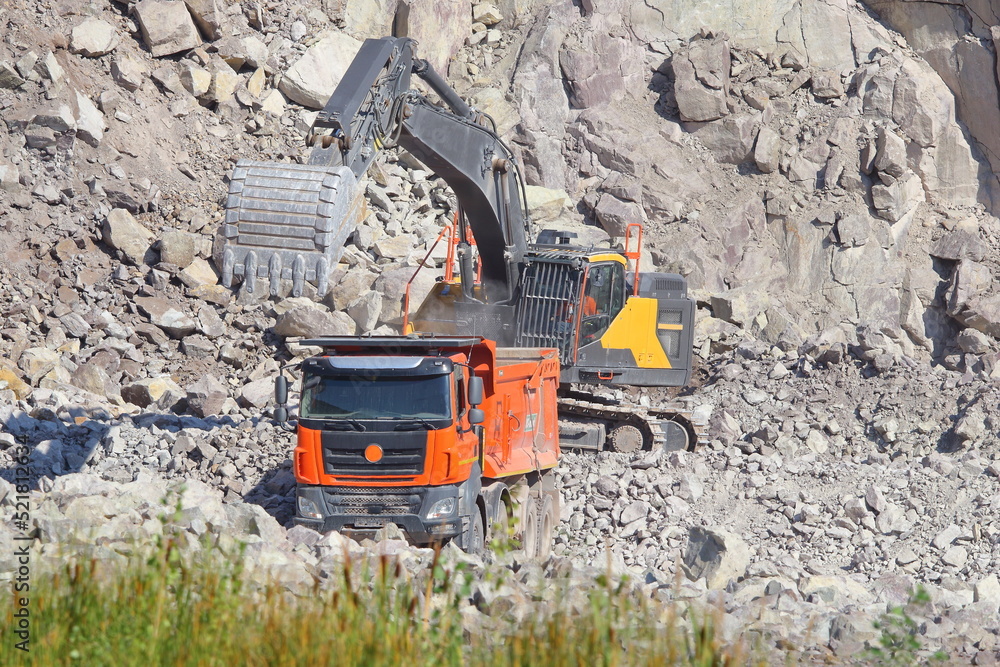 The yellow hydraulic crawler excavator loading stones into an orange truck in a stone quarry.  hydraulic crawler excavator and orange truck at work in a quarry.