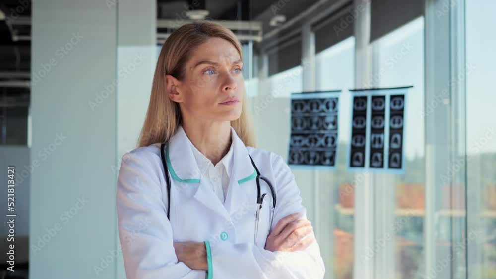Pensive young female caucasian doctor in white medical uniform look in window folding hands thinking or pondering, serious physician woman plan future career or success in medicine visualize. Pensive young female caucasian doctor in white medical uniform look in window folding hands thinking or pondering, serious physician woman plan future career or success in medicine visualize.