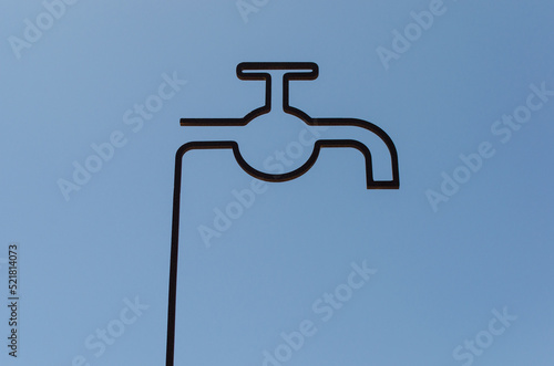 La silhouette di un rubinetto stilizzato in ferro battuto contro il cielo azzurro photo