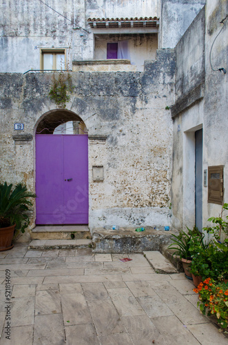 La porta viola in un tipico cortile dai muri bianchi in un borgo del Salento in Puglia