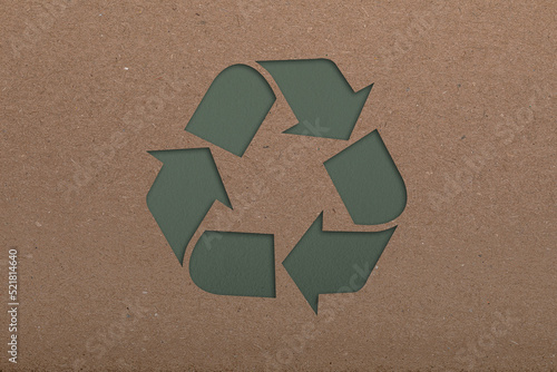 Sheet of cardboard with cutout recycling symbol on green background, top view
