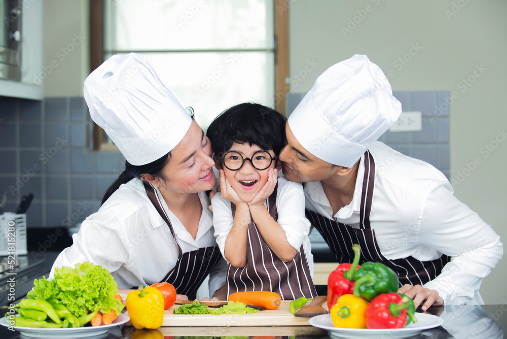 Happy Asian family wearing chef hat.apron cooking salad in kitchen at home Happy Asian family wearing chef hat.apron cooking salad in kitchen at home