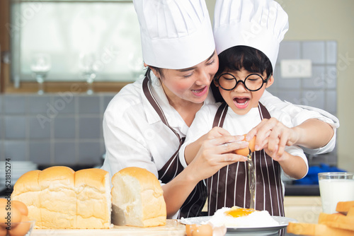 Cute asian boy with mother wearing chef hat  apron preparing for baking dough in kitchen at home photo