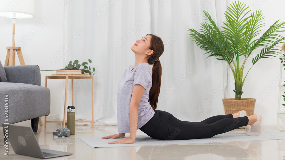 Yoga exercise concept, Asian woman doing yoga with lying in cobra pose and watching tutorial online Yoga exercise concept, Asian woman doing yoga with lying in cobra pose and watching tutorial online