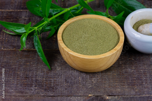 Andrographis paniculata powder in wooden bowl with mortar and pestle and green leaf on rustic wooden background.