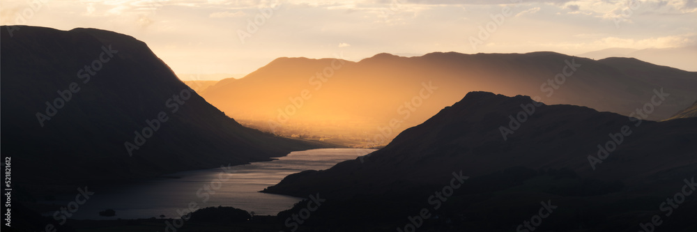 Beautiful golden light shining through shadow covered mountains. Crummock Water, Lake District, UK.