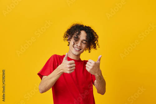 Cheerful funny Caucasian young man in red t-shirt show thumb up gesture posing isolated on over yellow studio background. The best offer with free place for advertising. Emotions for everyday concept