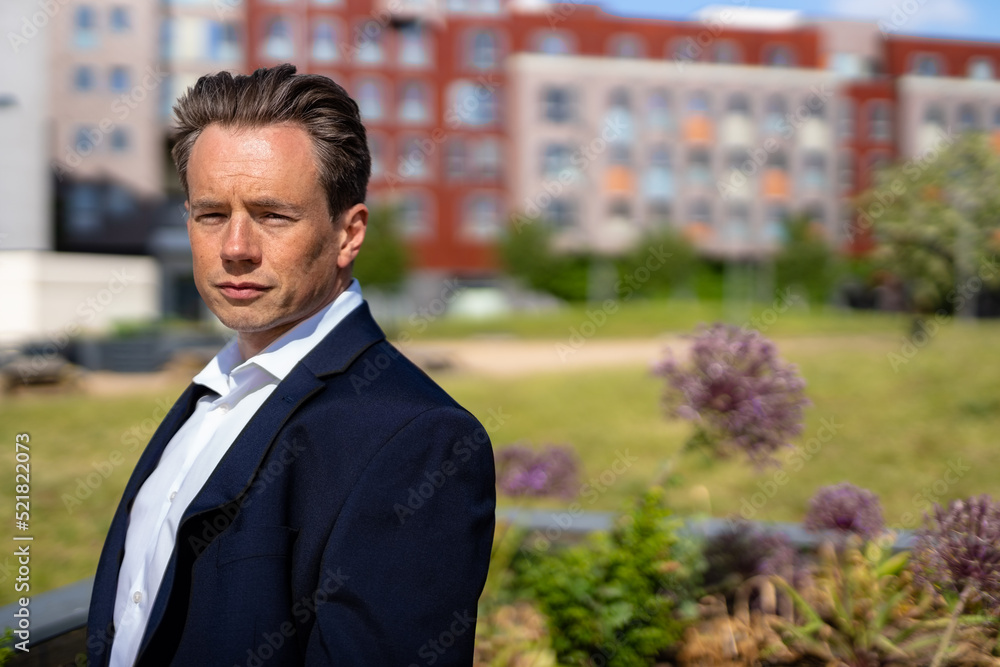 A handsome businessman in a casual dark blue suit in front of a residential area A handsome businessman in a casual dark blue suit in front of a residential area